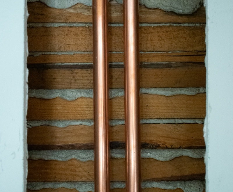 Two copper water pipes exposed inside a plaster-and-lath wall.